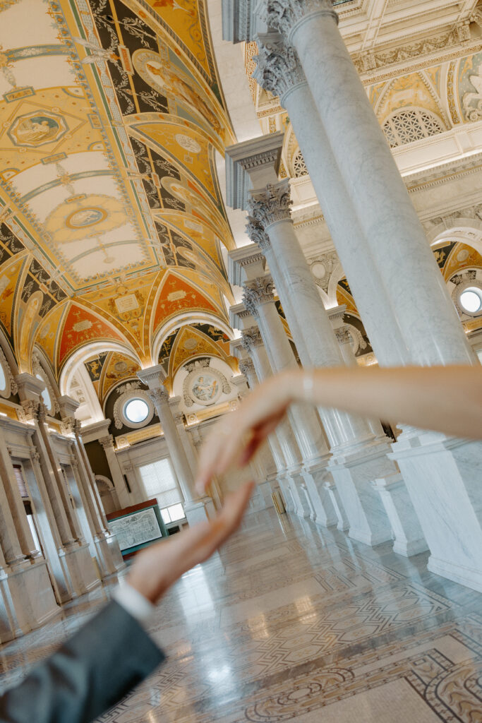 Detail shot of couple holding hands, highlighting the engagement ring and refined setting of the Library of Congress in DC.