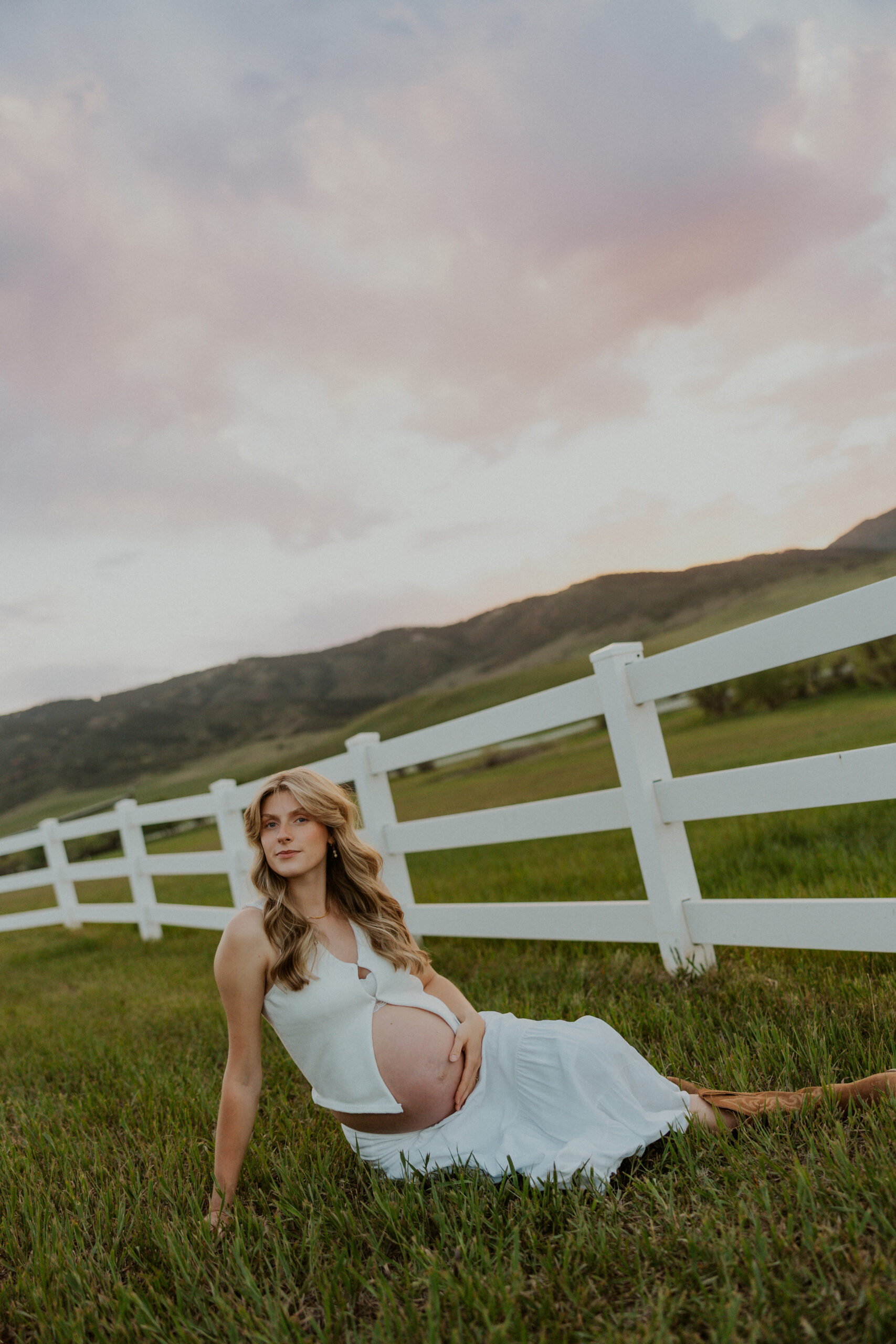 Pregnant woman in white dress and cowboy boots in countryside field
